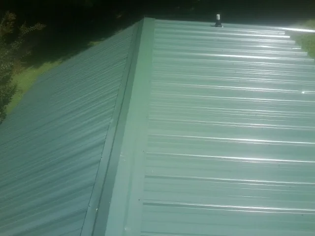 New green metal panels meeting at the ridge of a roof — Flat Roof Repair work by our crew in Utica
