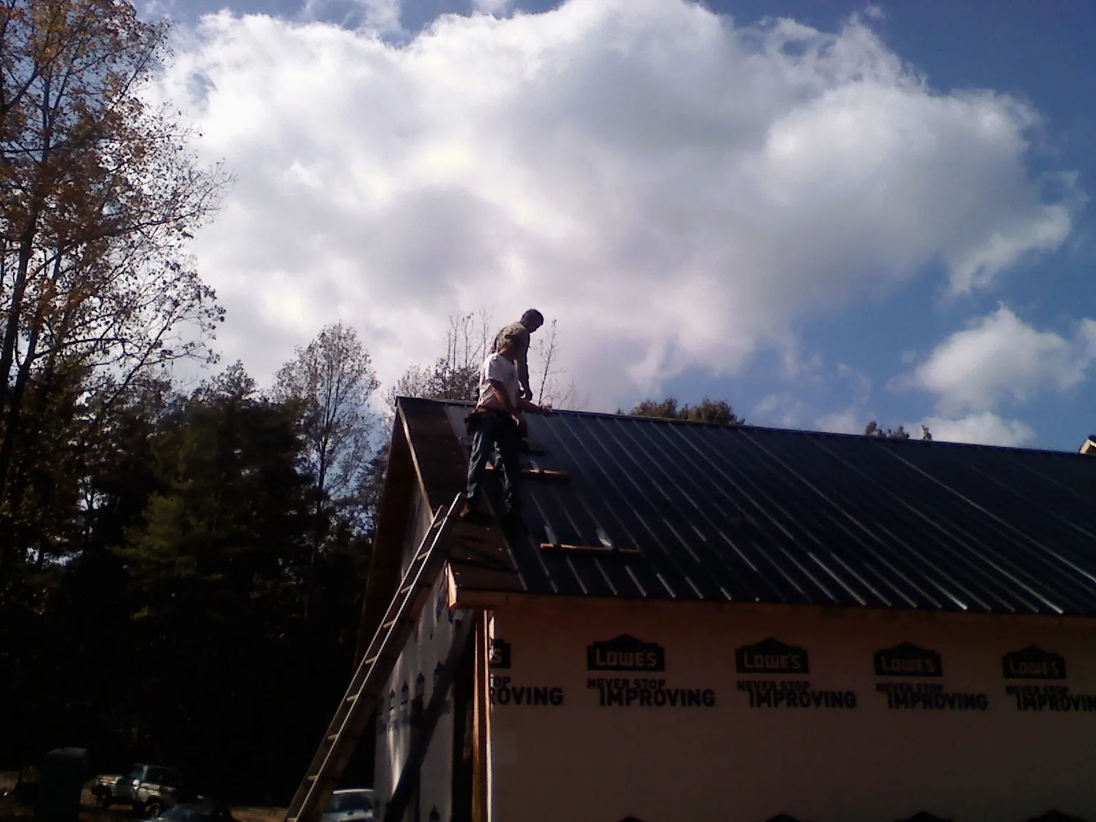 Roofer fastening dark metal panels high against a cloudy sky, from a Roof Inspection job in Utica